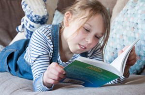 Deaf child lying on the sofa reading a book