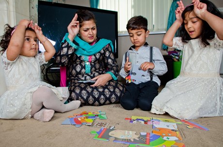 A mom and her three young children play a game in their living room while signing to each other.