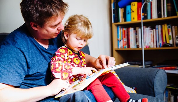 A dad reads a picture book with his young daughter who is wearing a cochlear implant.