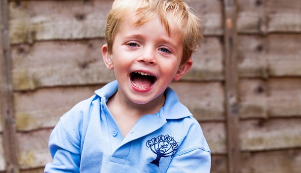 A young boy with hearing aids smiles at the camera. 