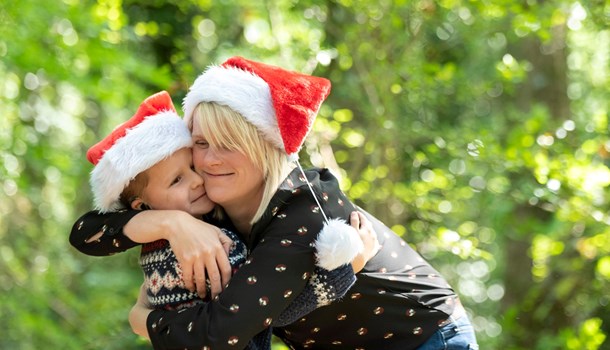 A young boy wearing a Santa hat hugging his mum in a wood.