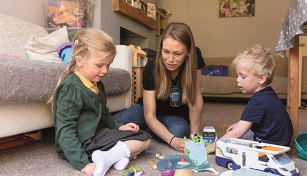A young girl in school uniform with rainbow cochlear implants playing on the floor with her mum and brother.