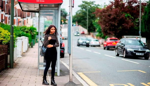 A deaf young person waiting by herself at a bus stop.