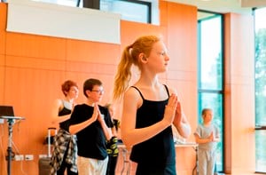 A child with a hearing aid practices dance in a studio with others.