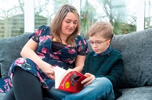 A deaf boy with microtia and a bone anchored hearing aid (BAHA) reading a book with his mum.