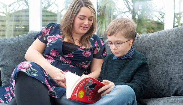 A deaf boy with microtia and a bone anchored hearing aid (BAHA) reading a book with his mum.