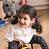 Holi wearing her cochlear implants clipped to her pigtails and playing on a bumblebee rocker.